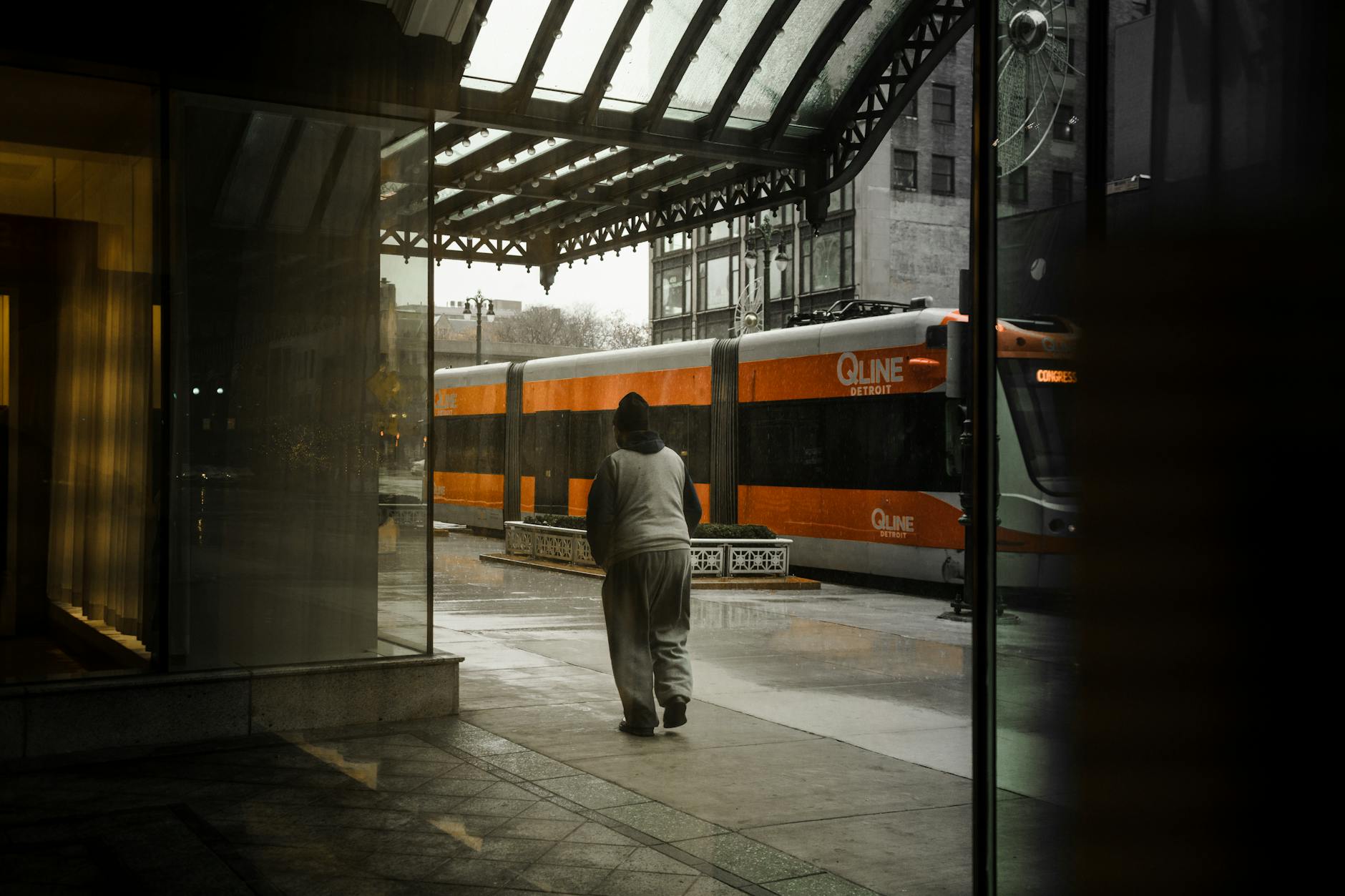 Pedestrian walking near a QLINE streetcar on a rainy Detroit evening